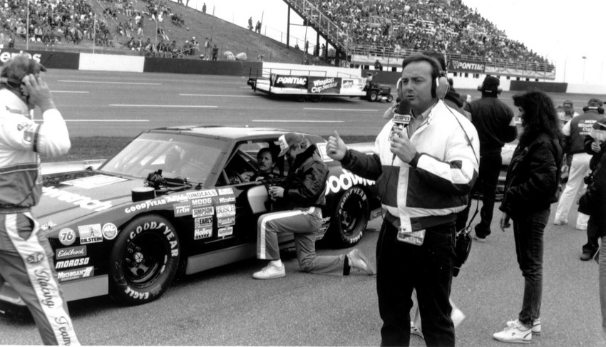 Dr. Jerry Punch provides commentary from track level in 1988 at North Carolina Motor Speedway. Behind him sits Dale Earnhardt in his car